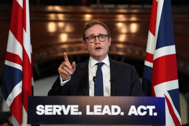 Tom tugendhat gives a speech flanked by two Union Jacks and behind a lectern with the slogan "Serve. Lead. Act."