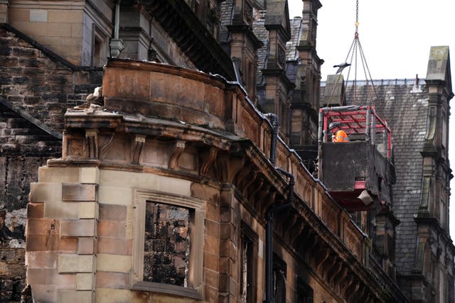 Workers in a cage suspended from a crane demolishing a building
