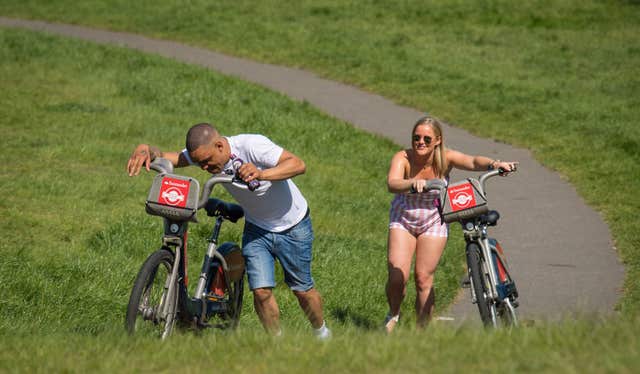 Two people struggle to push bikes up a steep hill in Greenwich Park, south London (Dominic Lipinski/PA)