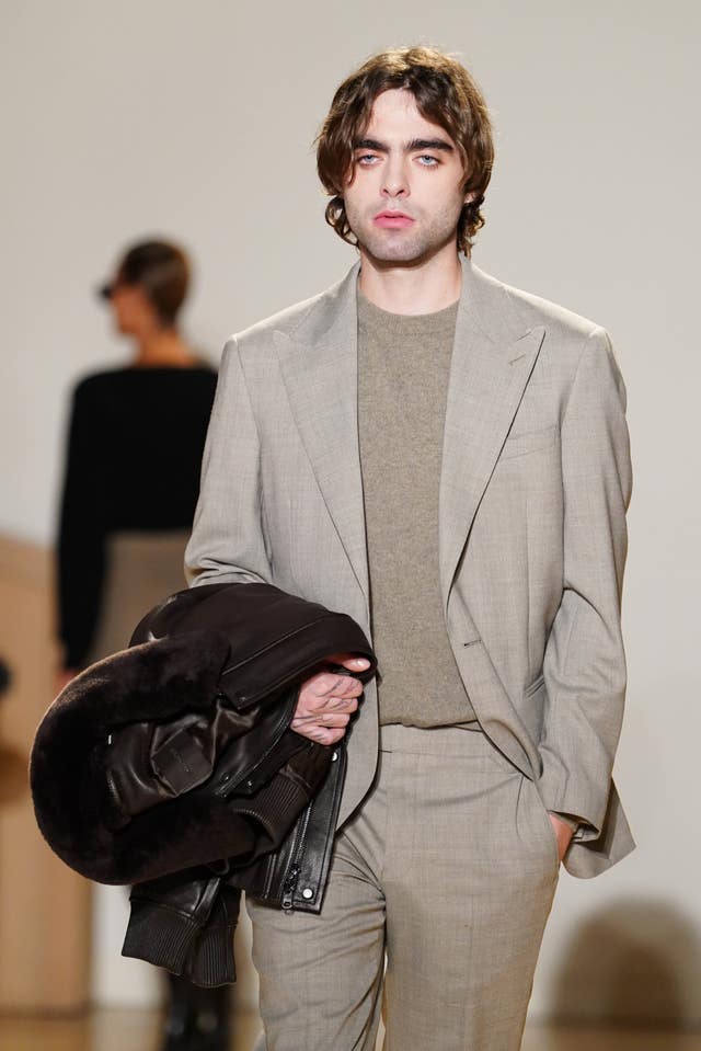 Lennon Gallagher wearing a grey suit holding a black jacket