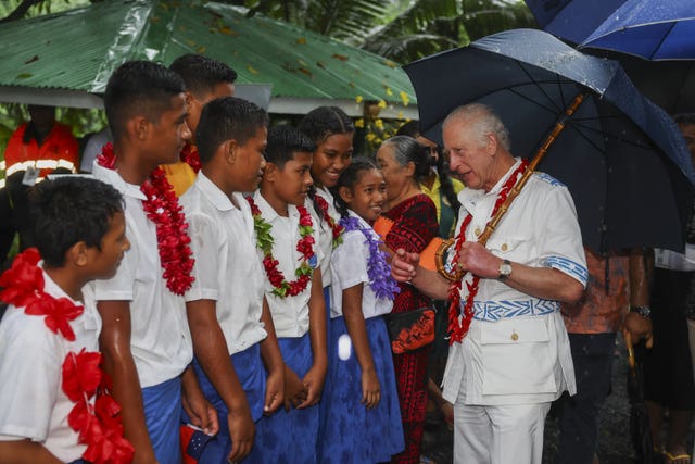 King sheltering under an umbrella while meeting local people