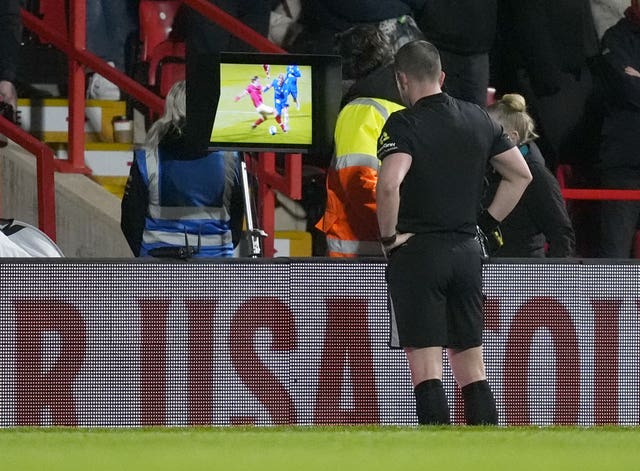 Referee Peter Bankes reviews a red card decision on a pitch-side screen