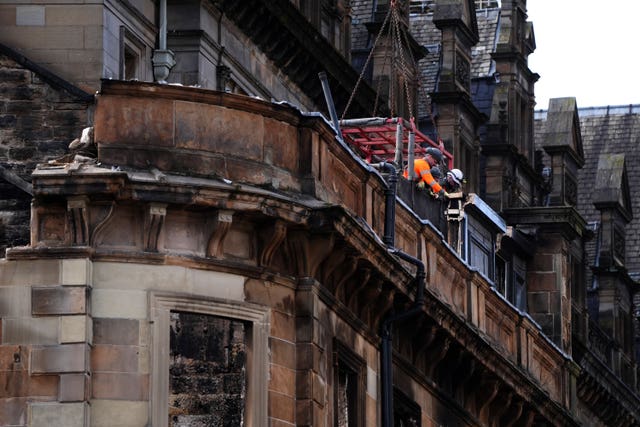 View of workmen in a basket beside the facade of a fire-damaged building
