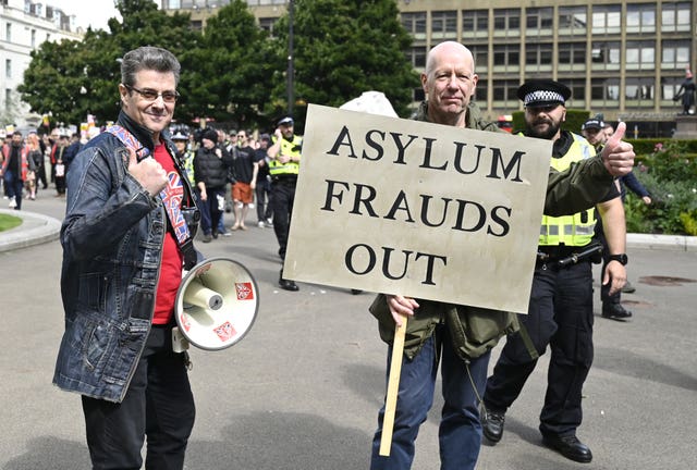 A man holding a sign saying 'asylum frauds out' next to another man with a megaphone