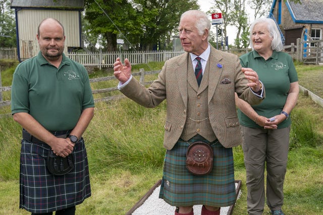 Charles, with hands raised, speaks while standing outside with two Flow Country staff