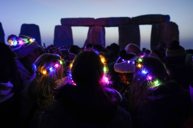 People gather as dawn breaks behind the stones at Stonehenge (Andrew Matthews/PA)