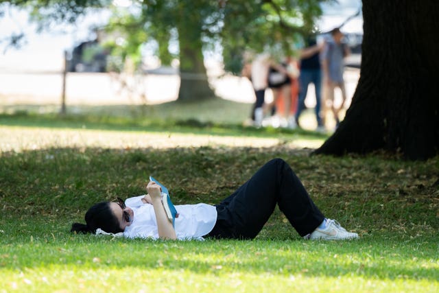 A person reads a book in Hyde Park, London during recent warm weather 