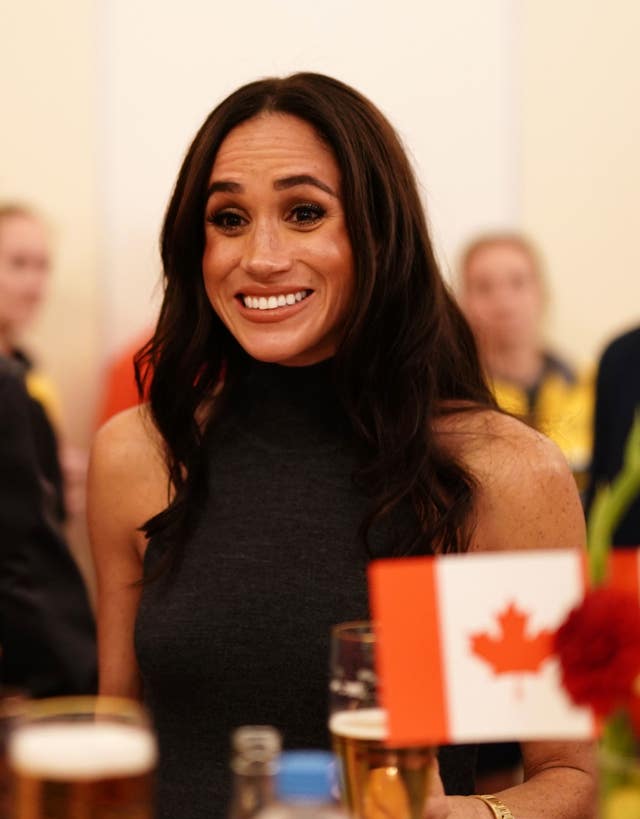 meghan gives a wide smile at the Invictus Games next to a Canadian flag