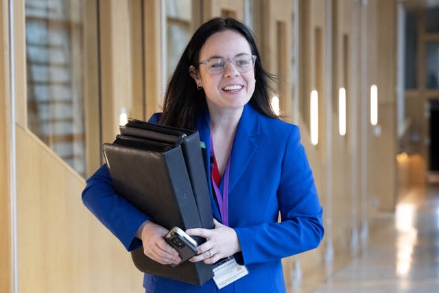 Kate Forbes smiling while walking through Parliament carrying a number of folders and phones