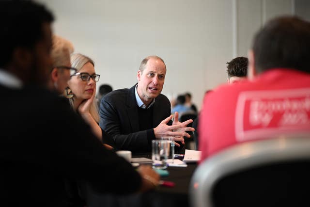 The Prince of Wales sitting at a table talking to a group of people