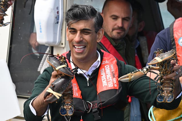 Rishi Sunak holds a lobster in each of his hands while wearing a life jacket on board a boat