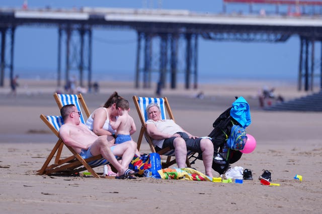 Three adults and a young child sitting on deckchairs during warm weather on Blackpool beach in Lancashire at the end of June