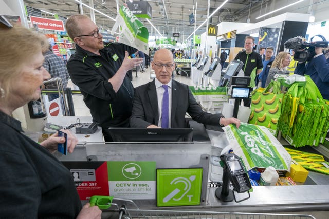 John Swinney mans an Asda store checkout with a member of staff standing alongside him