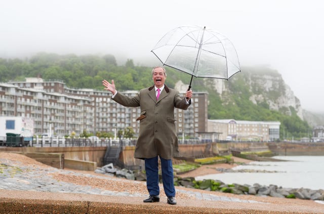 Nigel Farage stands in the rain with a see-through umbrella