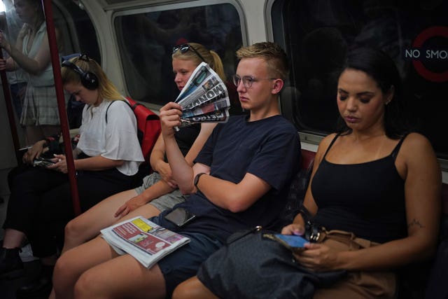 A man uses a newspaper as a fan while travelling on the Bakerloo line in central London during the heatwave