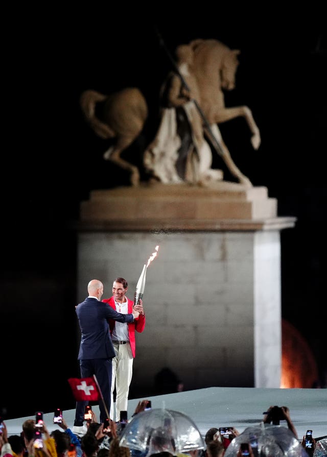 Zinedine Zidane, left, hands the Olympic Torch to Rafael Nadal