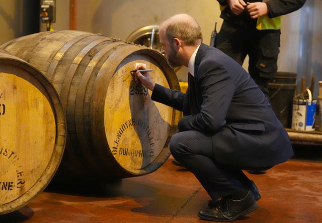 Jonathan Reynolds crouches down to sign a whisky cask