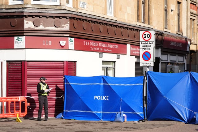 Police barriers blocking part of a street, with a policewoman manning the cordon