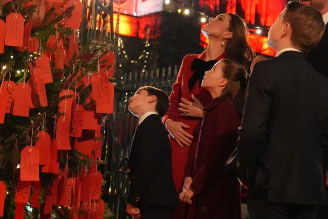 The Princess of Wales with her children Prince George, Princess Charlotte and Prince Louis look at messages on the Kindness Tree ahead of the Together At Christmas carol service at Westminster Abbey 