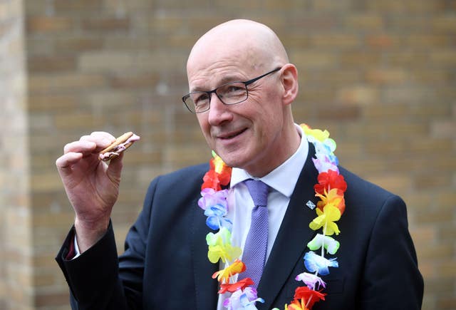 Scottish First Minister and SNP leader John Swinney wearing a colourful garland and holding a biscuit during a visit to the Jeely Piece Club in Glasgow