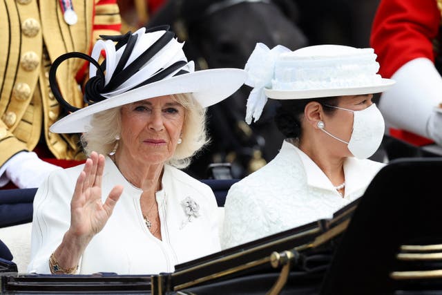 Camilla, wearing a white dress and hat, waves during the procession to the palace