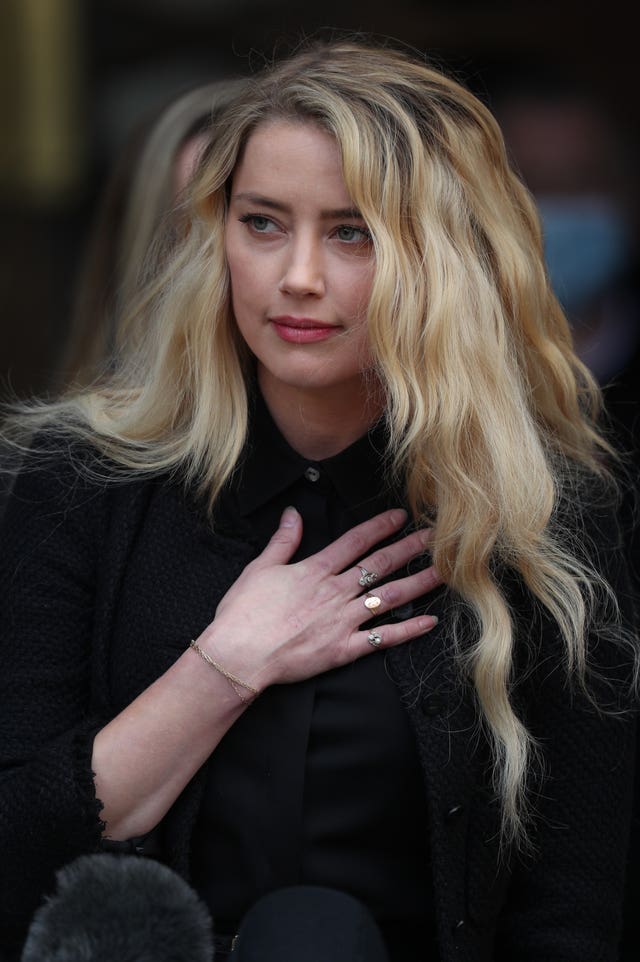 Amber Heard dressed in black, with one hand resting on her chest