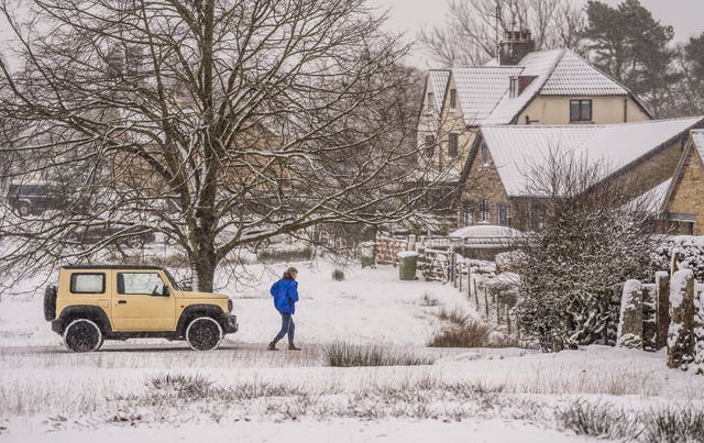 A yellow car and a woman walking pictured in the snow