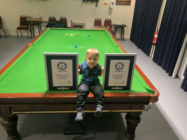 Jude Owens sits on a snooker table with his record-breaking certificates