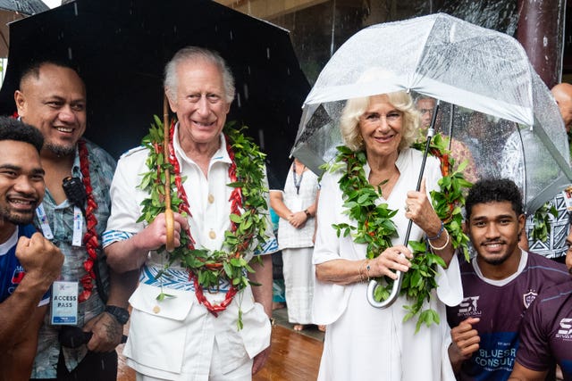 Charles and Camilla hold umbrellas as they meet members of the Apia rugby team during a visit to the Samoan Cultural Village in Apia