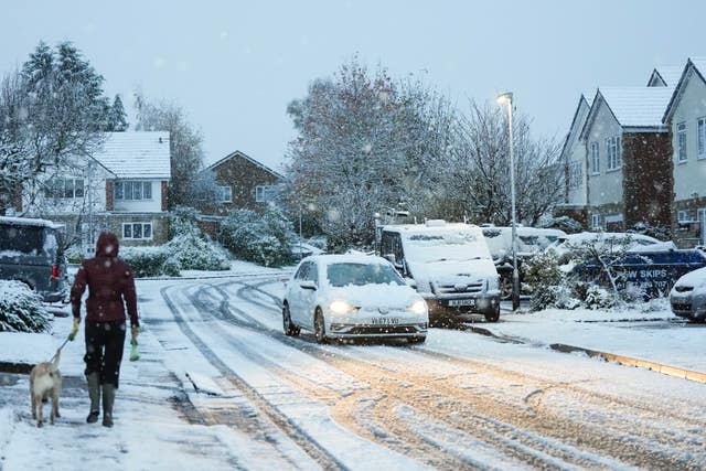 A person walks a dog along a snowy street in Warwick