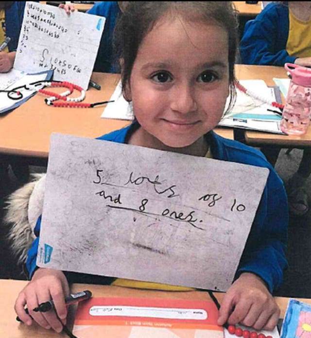 Sara Sharif smiling in a classroom and holding up her schoolwork