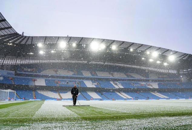 Manchester City head groundskeeper Lee Jackson sweeps snow off the pitch