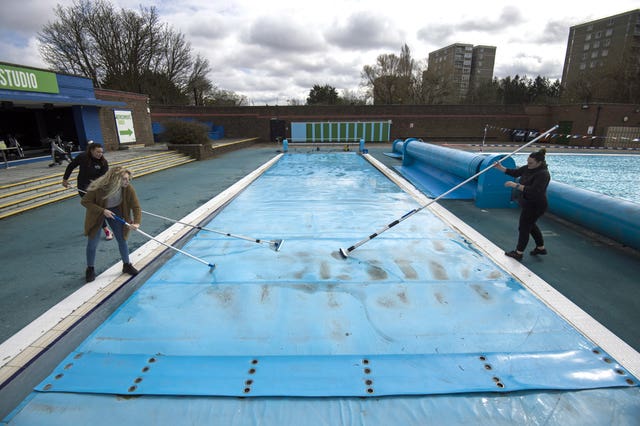 Members of staff clean the cover of the pool during pre-opening preparation and cleaning of Charlton Lido, south London (Kirsty O'Connor/PA)