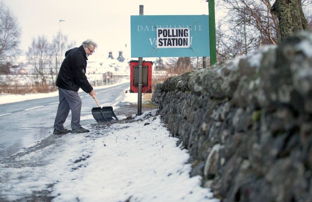 A man clears snow outside the polling station at the village hall in Dalwhinnie in the Cairngorms