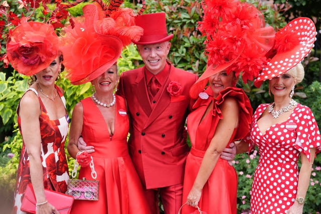 A man in a red suit poses with women wearing red hats