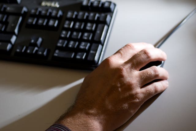 A hand on a mouse next to a keyboard