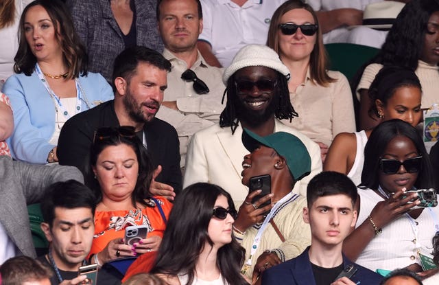 Kojey Radical sitting beside Sabrina Elba in the Wimbledon crowd