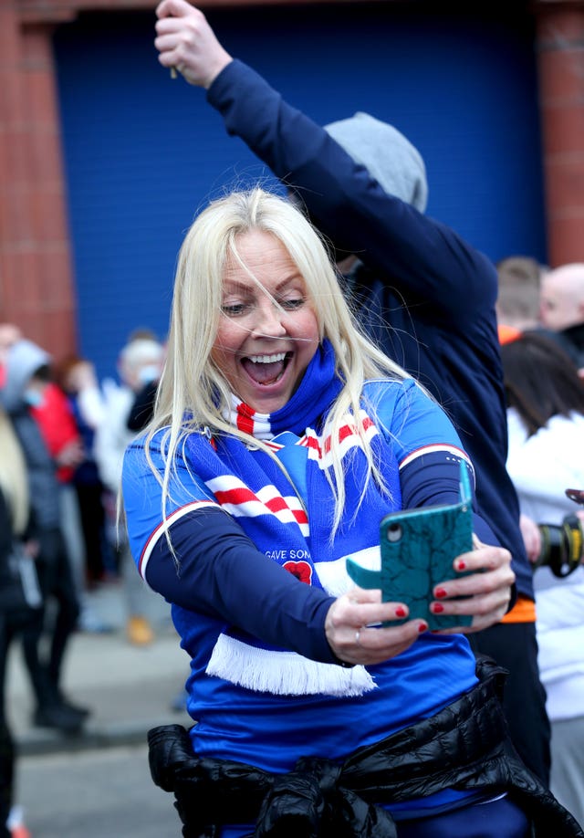 A Rangers fan celebrates by taking a photo outside Ibrox