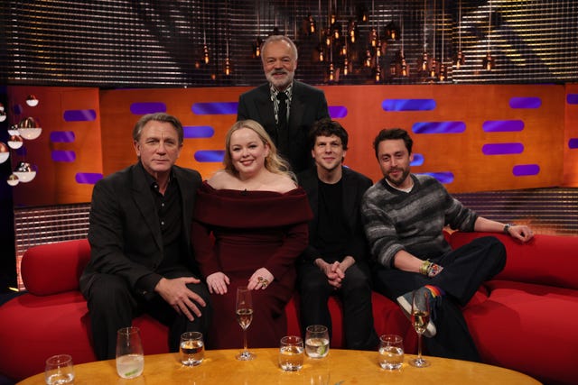 Graham Norton standing behind Daniel Craig, Nicola Coughlan, Jesse Eisenberg and Kieran Culkin, who are seated on the couch for The Graham Norton Show