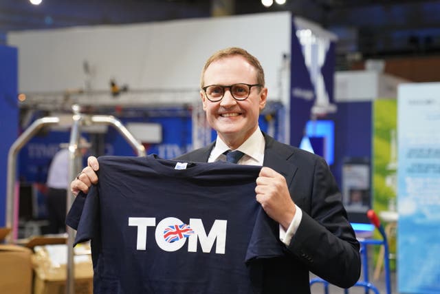 Tom Tugendhat smiling while holding up a T-shirt reading 'Tom'