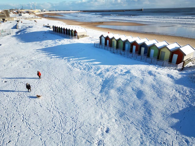 People walk their dogs through the snow beside the beach huts at Blyth in Northumberland
