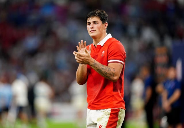 Welsh former rugby player Louis Rees-Zammit, wearing red Wales shirt and white shorts, applauds 