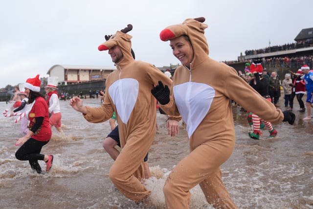 Two swimmers in reindeer costumes run for the waves 