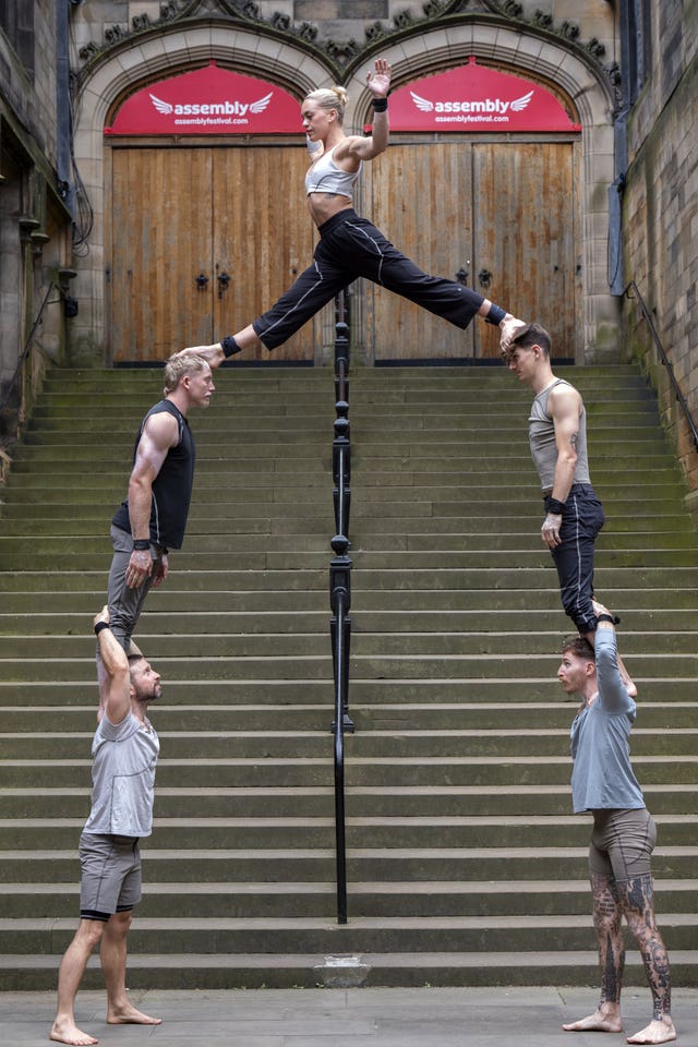 Two acrobats standing on the shoulders of another two acrobats while a female acrobat balances a foot on each of their heads in front of the Assembly Hall in Edinburgh