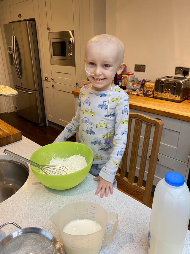 A little boy stands at a table with a food mixing bowl  