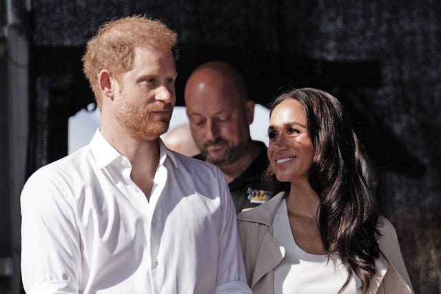 Meghan looks sideways towards Harry and smiles, with both wearing white tops