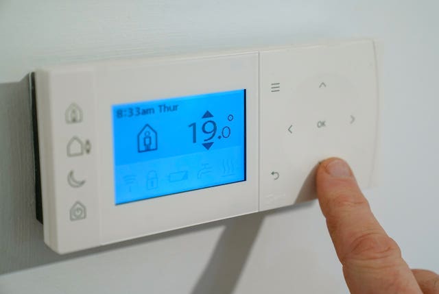 A homeowner turns down the temperature of a central heating thermostat