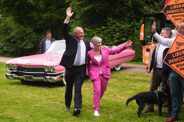 Sir Ed Davey and Daisy Cooper wave at supporters while walking in front of a pink car