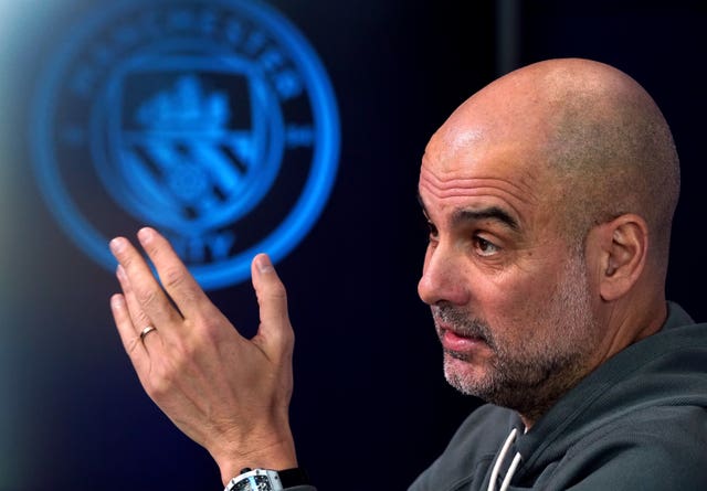 Pep Guadiola gestures while sitting in front of a Manchester City crest