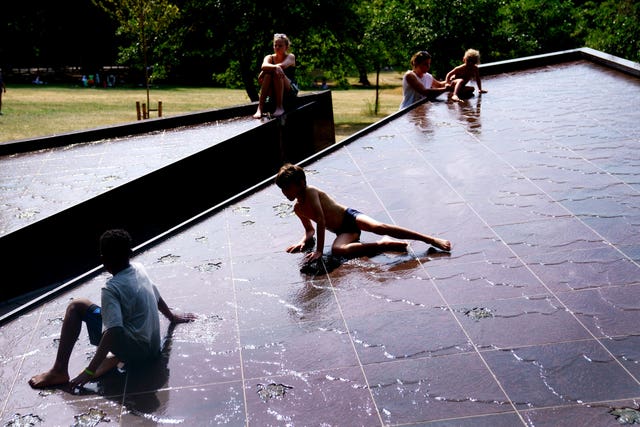 Young children play in the Canada Memorial fountain during warm weather in Green Park, central London